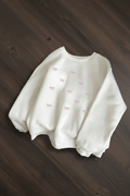 Suéter blanco con lazos rosas sobre madera oscura